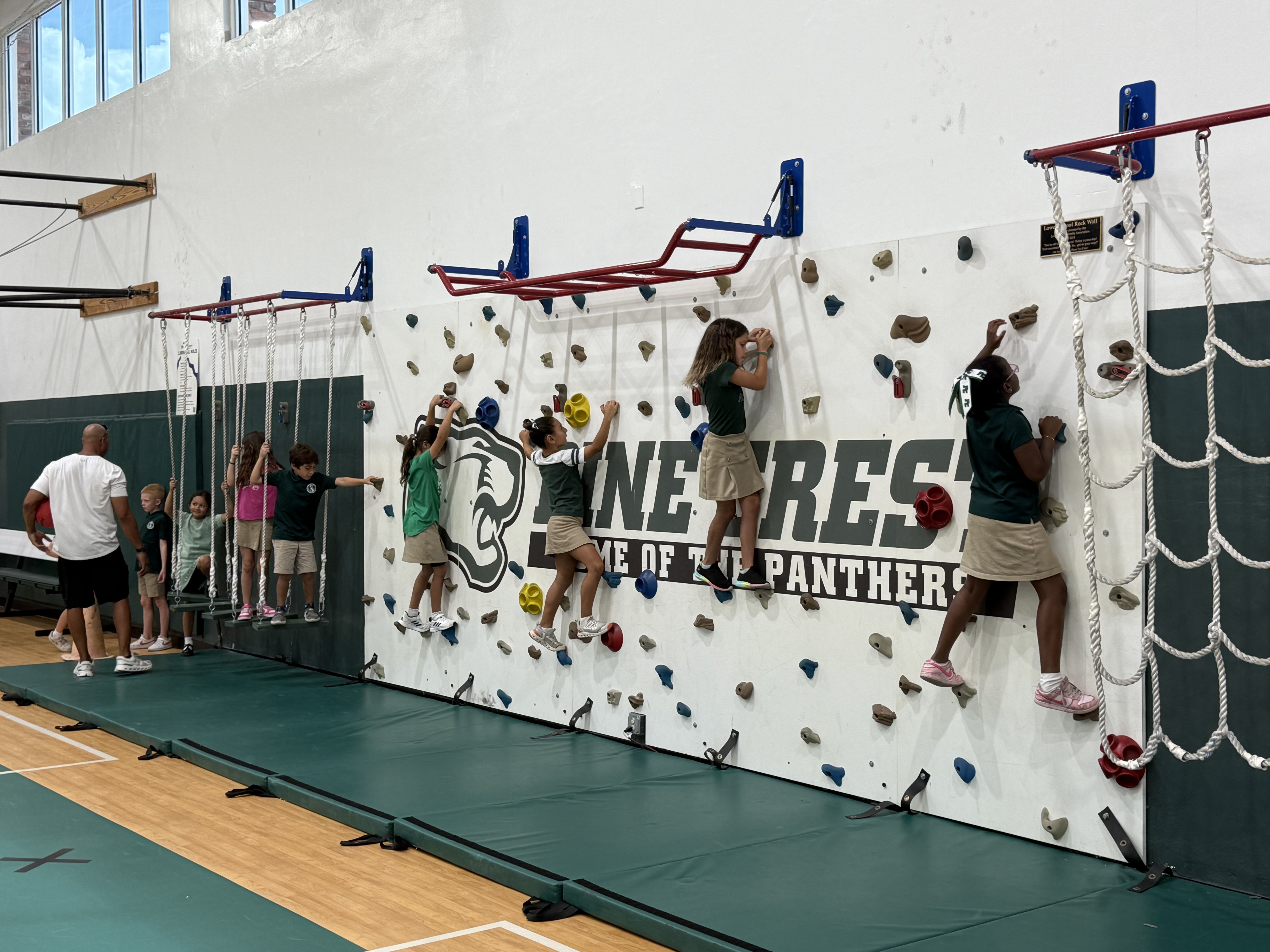 Lower School students climb the rock wall during physical education class